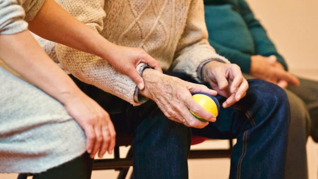 A person wearing a sweater holds a ball, while another person's hand rests on their arm, offering support.
